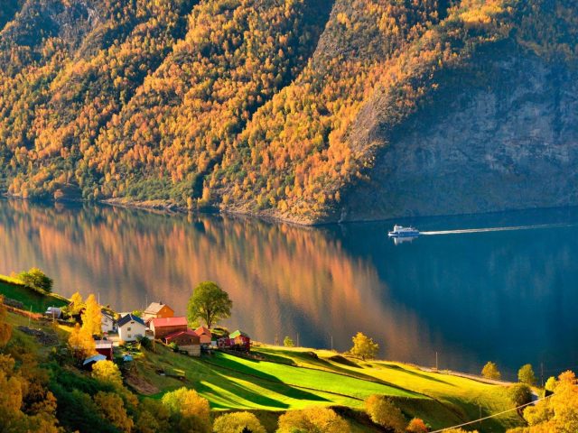 Дома на склоне зеленых покрытых гор и бело-синяя лодка на водоеме рядом с зелеными и желтыми покрытыми горами природа