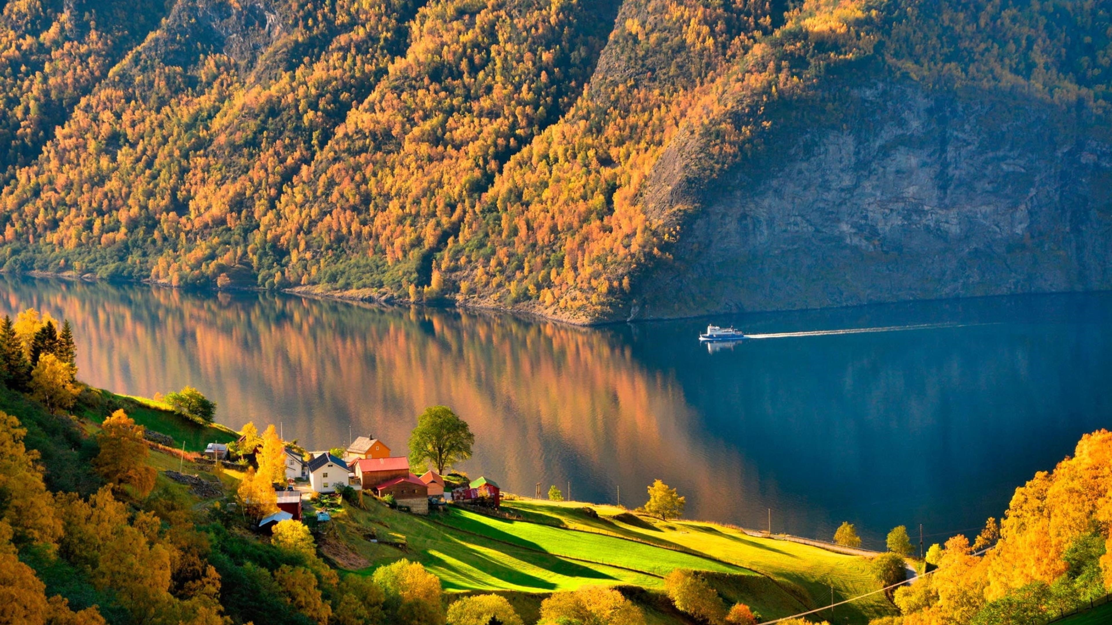 Дома на склоне зеленых покрытых гор и бело-синяя лодка на водоеме рядом с зелеными и желтыми покрытыми горами природа обои скачать