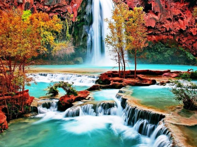 Водопад между покрытыми водорослями скалами льется по ручью реки в окружении разноцветных деревьев природы