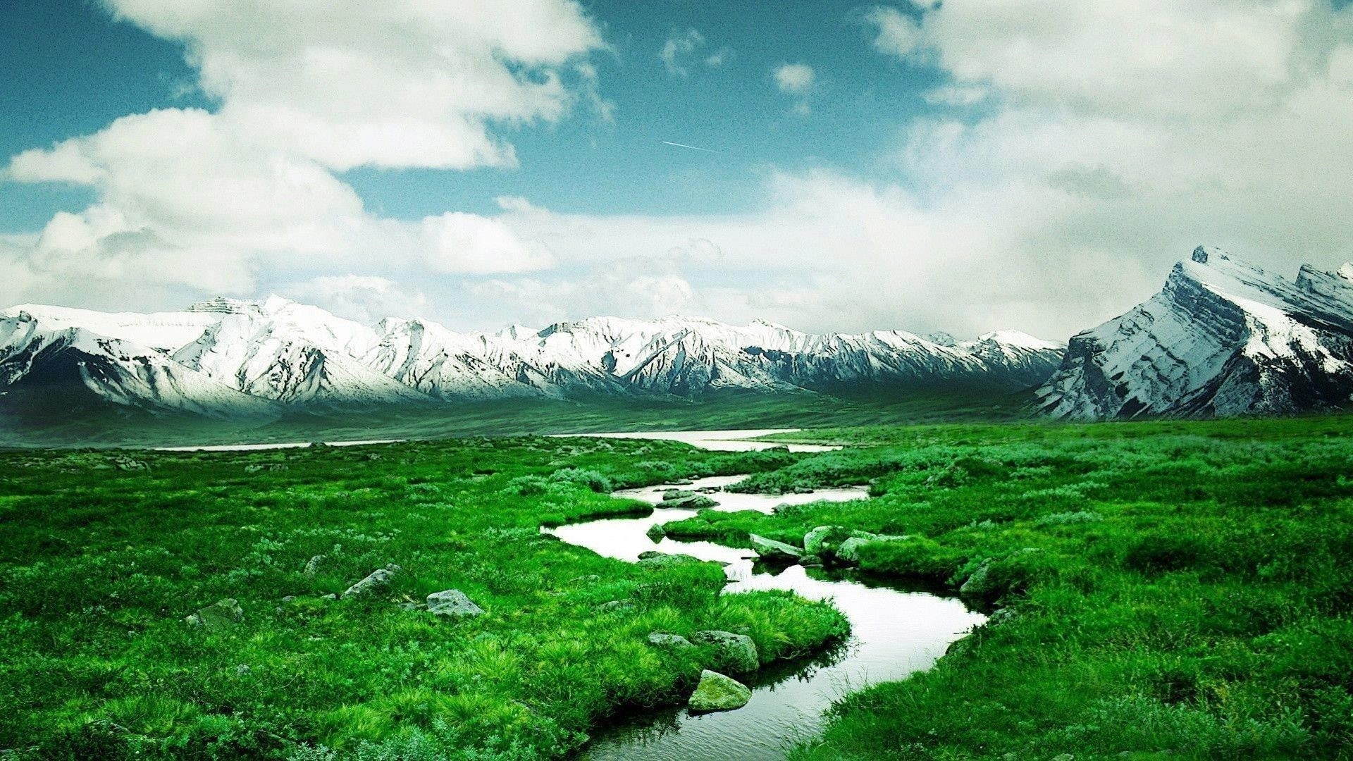Река между лугами и пейзажем вид на заснеженные горы под облачным небом природа обои скачать