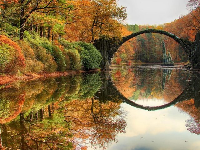 Дьявольский мост посреди реки в лесу с отражением окруженной цветущими деревьями природы