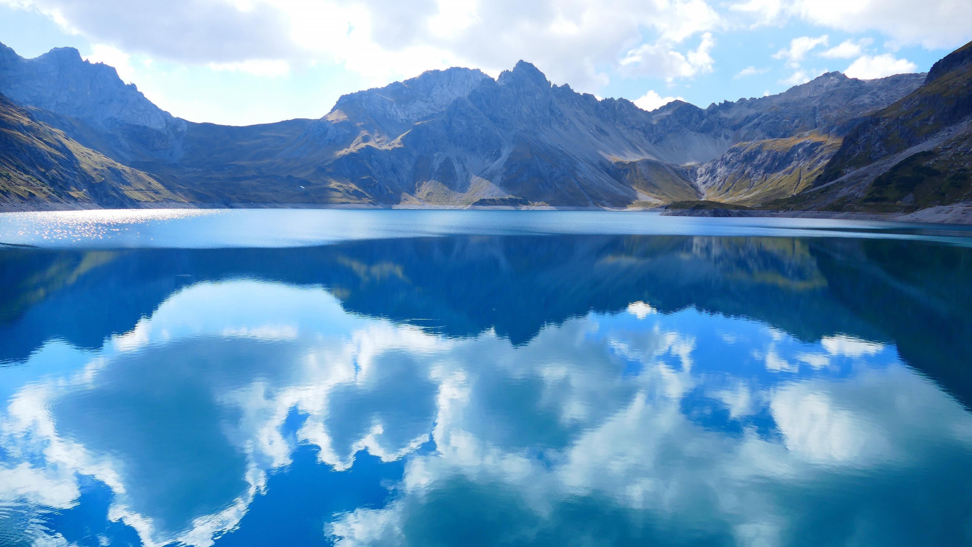 Бело - зеленые покрытые горы под облачным голубым небом рядом с озером с отражением природы обои скачать