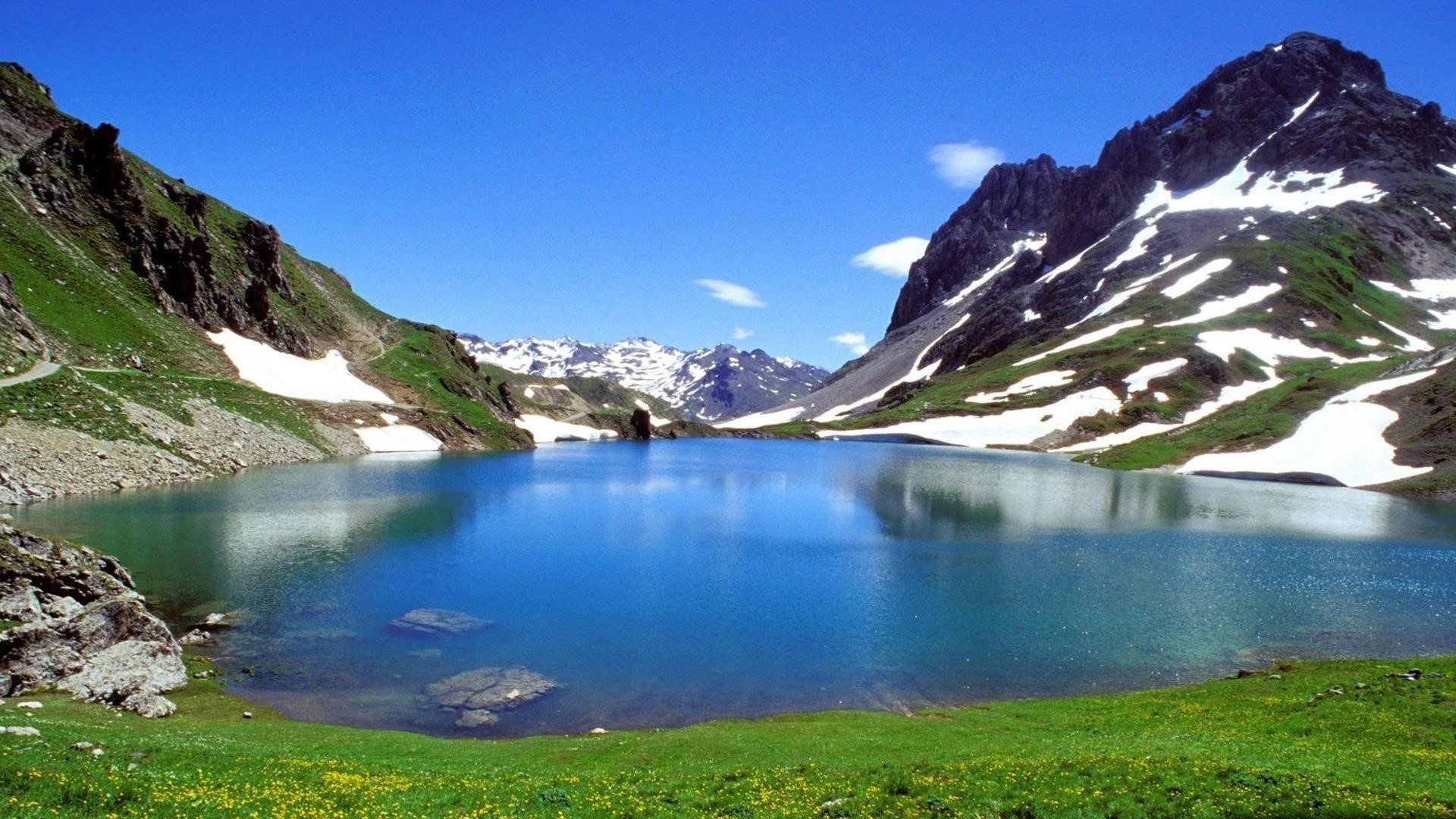 Озеро между белыми черно зелеными покрытыми горами днем под голубым небом природа обои скачать