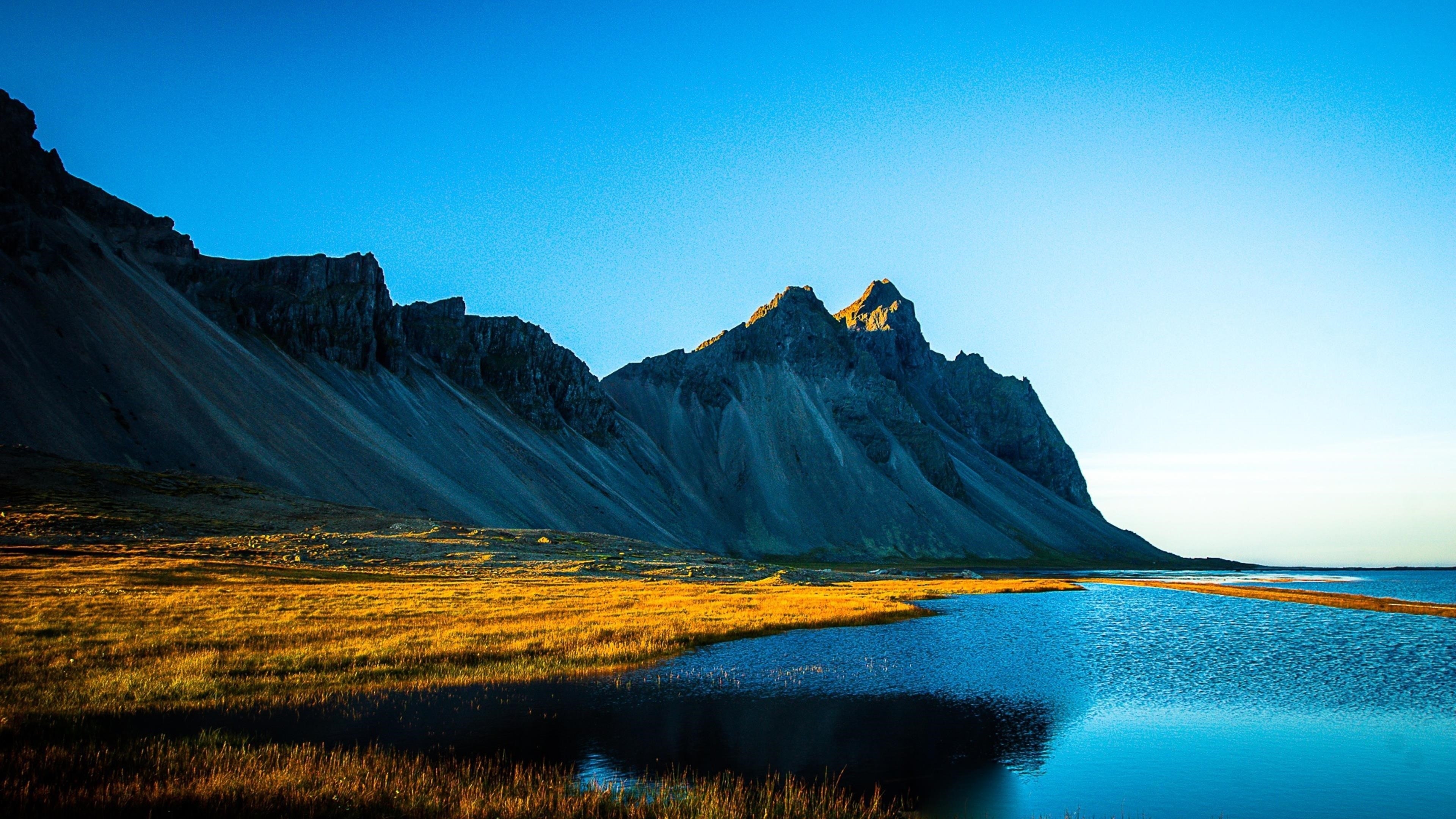 Покрытое травой озеро рядом с белой покрытой горой под голубым небом в дневное время природа обои скачать