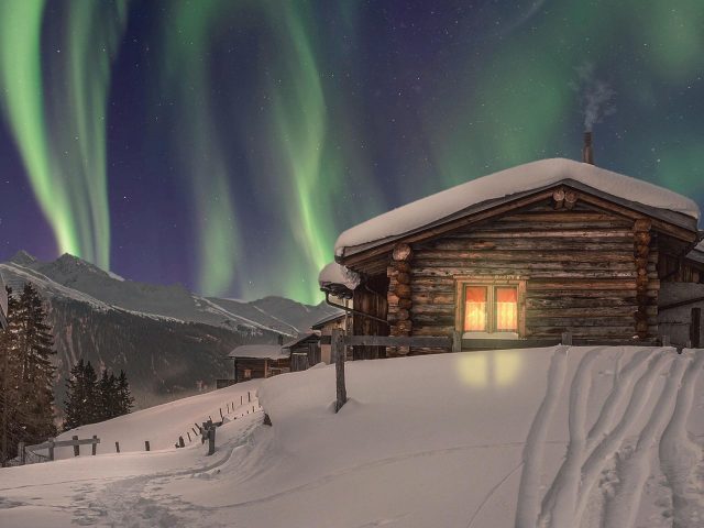 Заснеженный дом в северном сиянии зимой Зимой